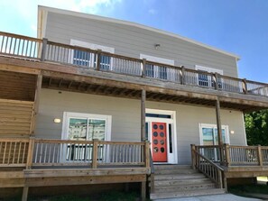 A two-story building with a balcony, a red door, and a wooden deck. - Whale of a Time offers a thoughtfully designed space (Galveston)