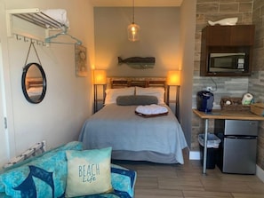 A compact room with a bed, a small seating area, a kitchen with a microwave and refrigerator, and a hanging light fixture. - Whale of a Time offers a thoughtfully designed space (Galveston)