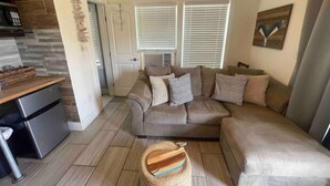 A living room with a sofa, a small table, a kitchen area, and a door leading to another room. - Whale of a Time offers a thoughtfully designed space (Galveston)