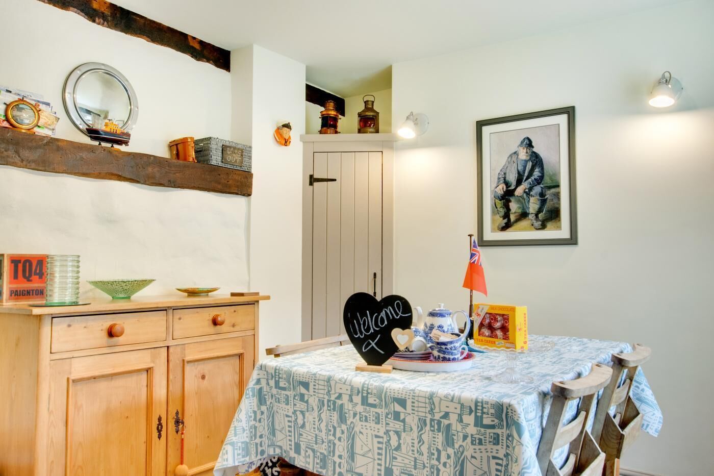 Een eetgedeelte met een tafel voor twee personen, een kast met lades, een spiegel en een ingelijste foto aan de wand.