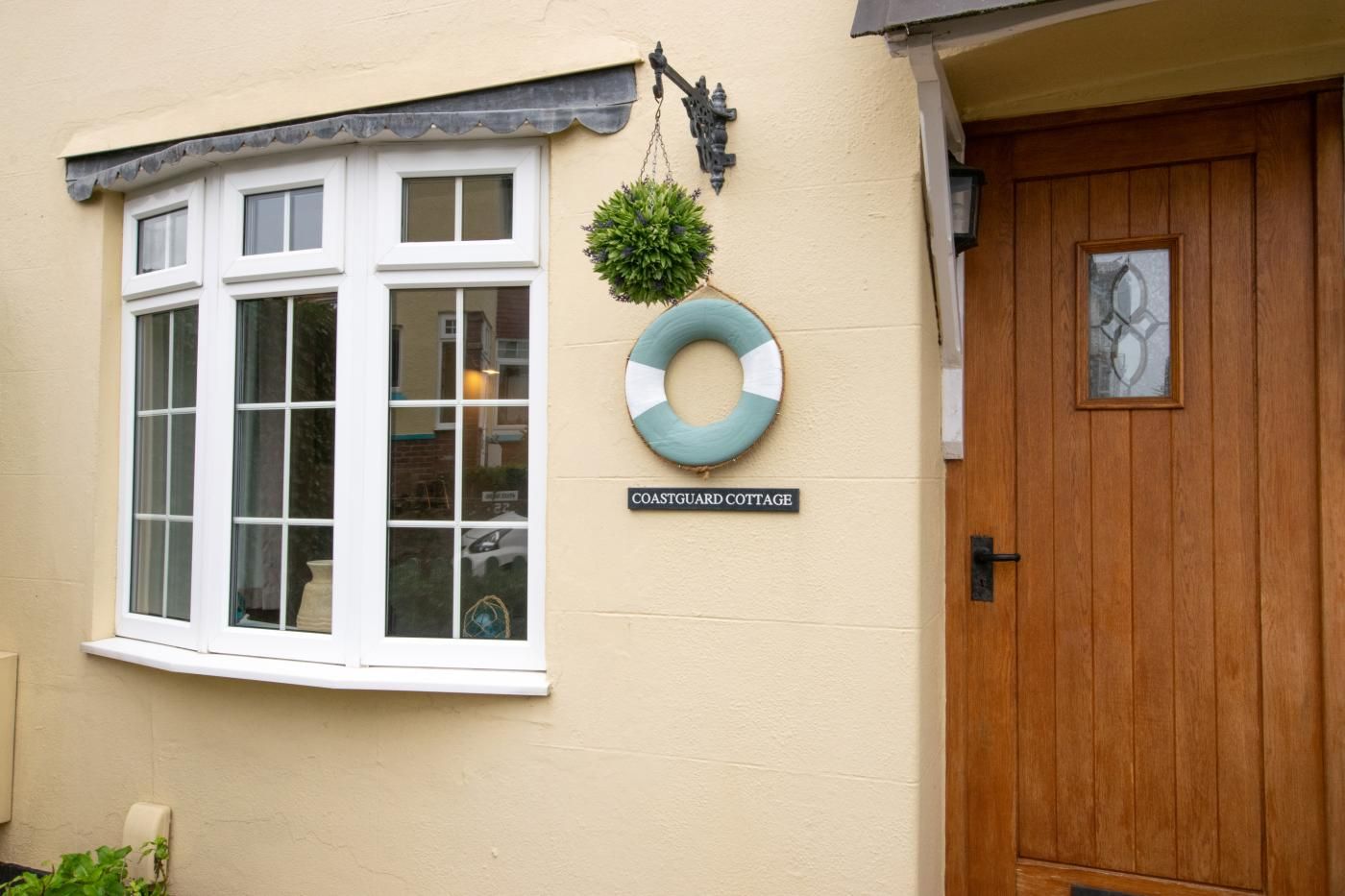 Une petite maison avec une baie vitrée, une porte en bois et une pancarte indiquant : « MAISON DU SERVICE DE SURVEILLANCE CÔTIÈRE ».