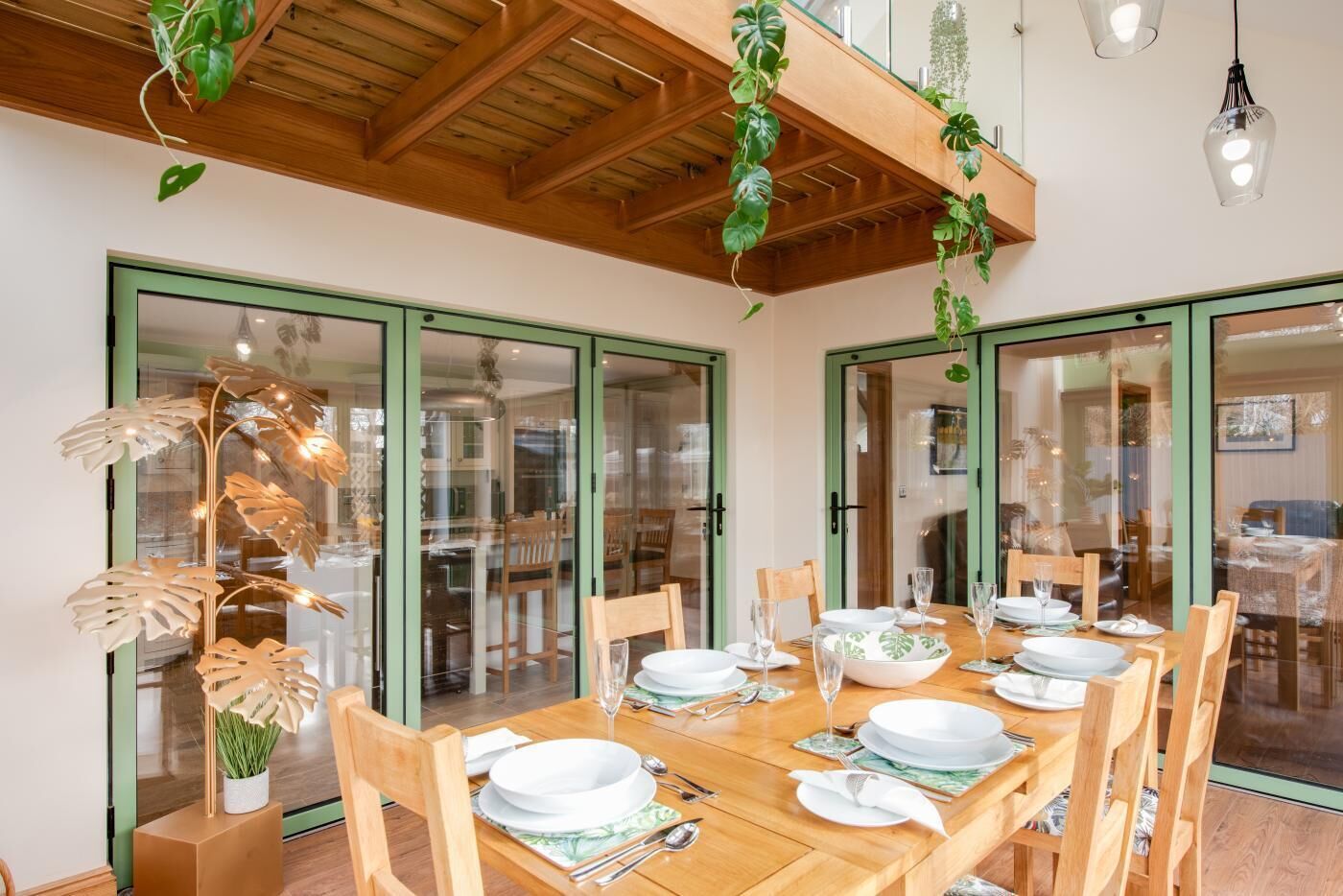 A dining area with a wooden table set for six, surrounded by chairs, with glass doors leading to another room.