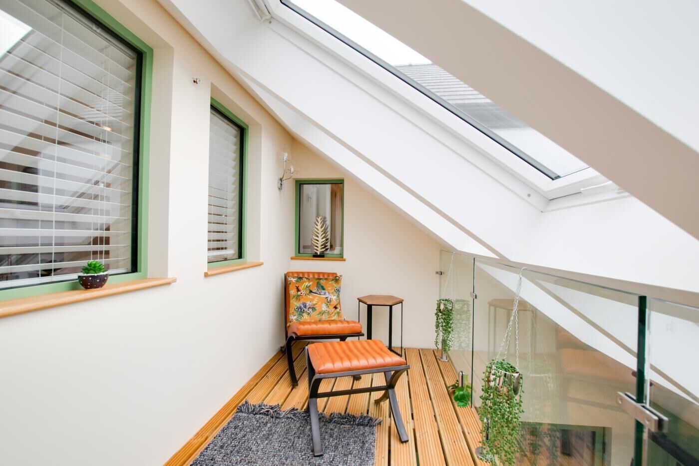 A small balcony with a wooden floor, a chair, a small table, and a potted plant.