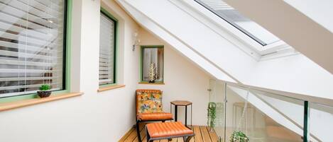 A small balcony with a wooden floor, a chair, a small table, and a potted plant.