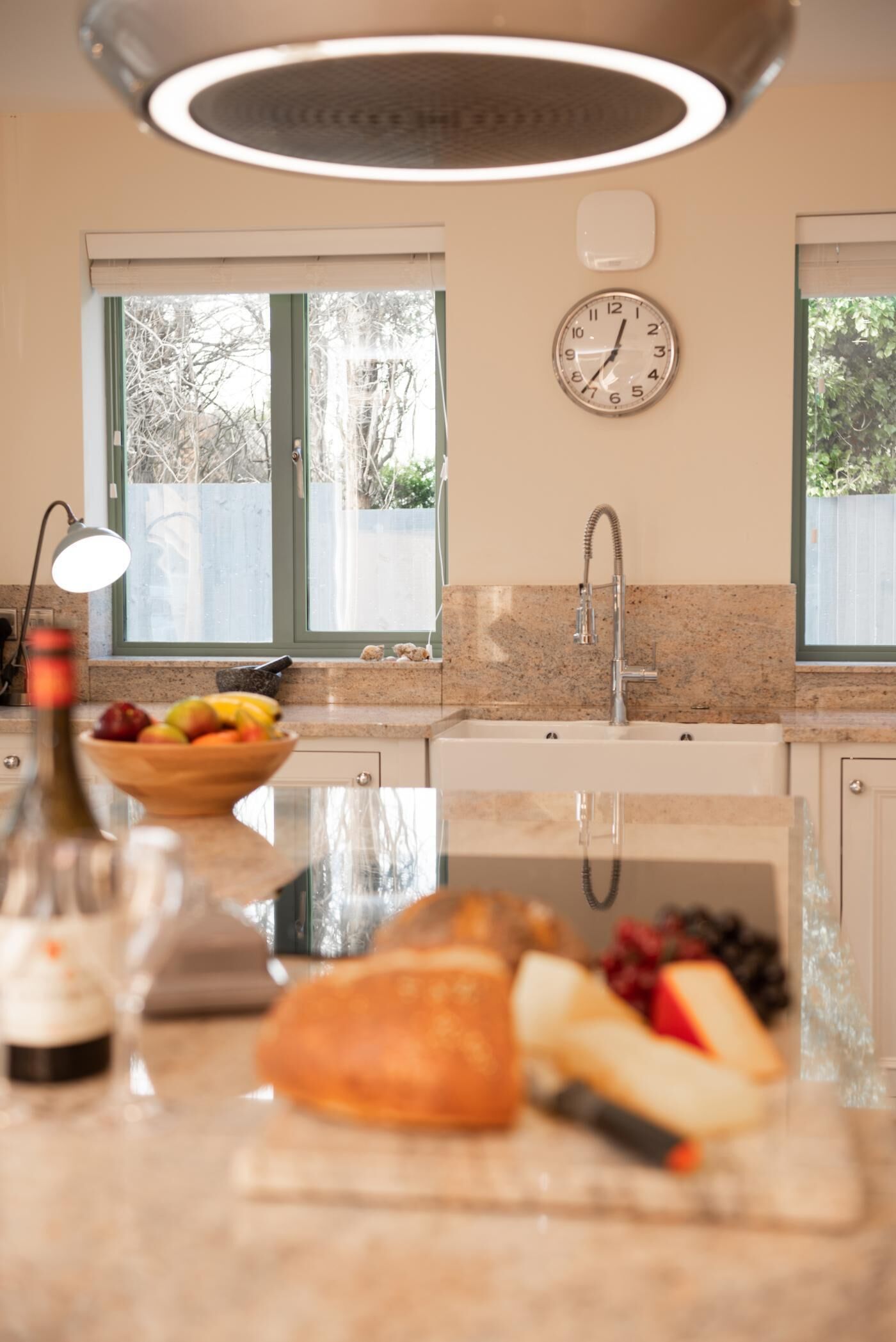 A kitchen with a window, a clock, and a fruit bowl on the counter.