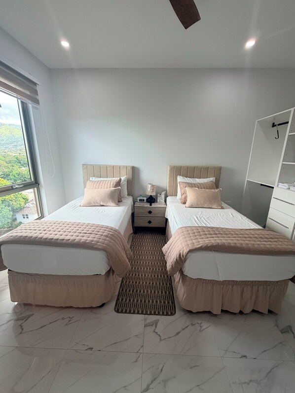 A hotel room with two beds, a nightstand, a mirror, and a view of the outdoors.