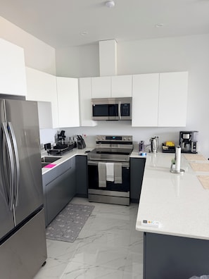 A modern kitchen with stainless steel appliances, white cabinetry, and a marble floor.