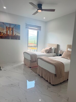 A bedroom with two beds, a ceiling fan, a window with a view, and a marble floor. - 2BDRM • 24hrs Security • Top floor with Mountain View • Rooftop Pool and Gym (Kingston)