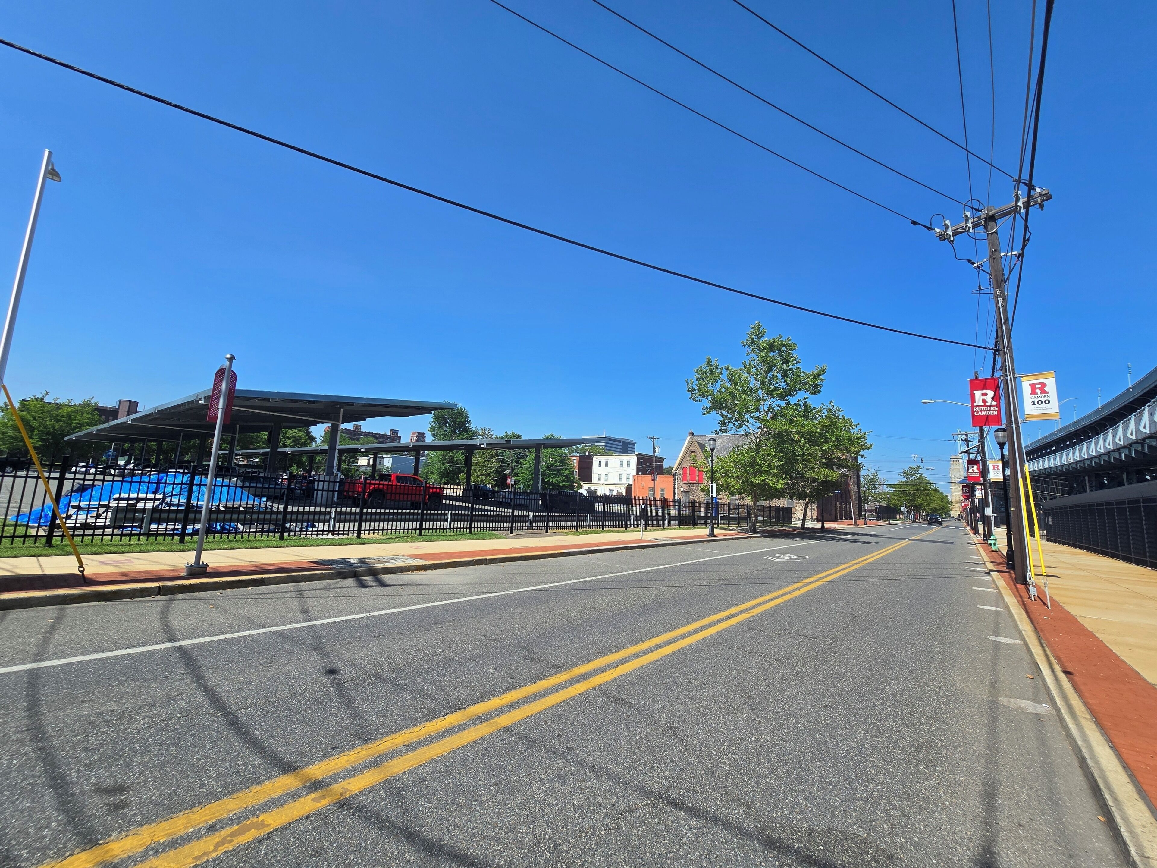 A clear road with a double yellow line, a covered parking area, and a building with a red roof.