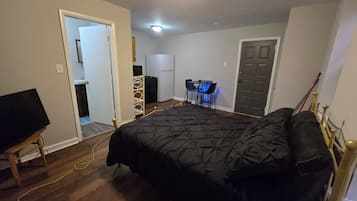 A bedroom with a bed, a desk with chairs, a television, and a door.