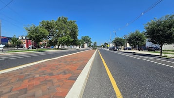 A wide street with a brick sidewalk, trees, and parked cars.