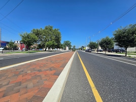 Una amplia calle con aceras de ladrillo, árboles y coches estacionados.