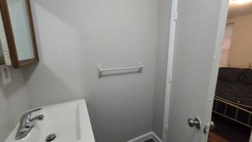 A bathroom with a sink, mirror, towel rack, and a door leading to another room.