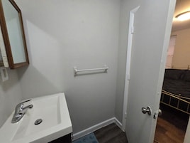 Un baño con lavamanos, espejo, toallero y puerta que da a otra habitación.