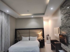 Habitación de hotel moderna con una cama grande, una mesita de noche, un refrigerador pequeño, un televisor montado en la pared y una pared con diseño de mármol.