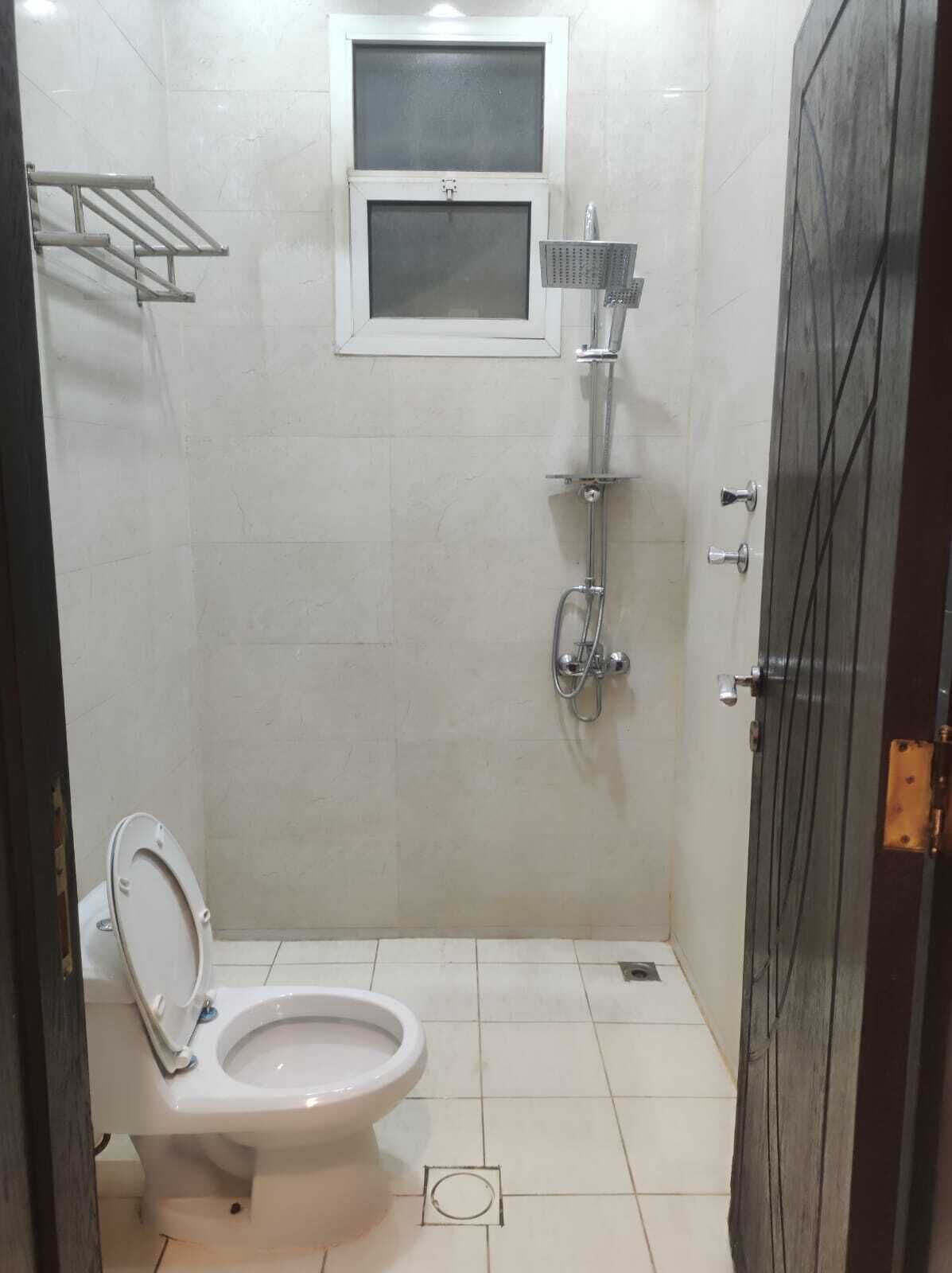 A small, tiled bathroom with a toilet, a shower, and a window.