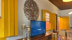 Ein Wohnzimmer mit Fernseher auf einem Holzschrank, gelben Wänden und einer dekorativen Wandgestaltung.