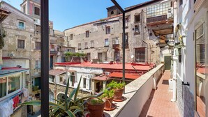 Un balcon agrémenté de plantes en pot, une vue sur les immeubles voisins et un ciel dégagé.