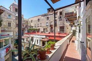 Ein Balkon mit Blumentöpfen, Blick auf benachbarte Gebäude und einen klaren Himmel.