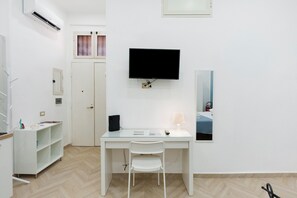 Ein Hotelzimmer mit Schreibtisch, Stuhl, Fernseher und einem Bett mit blauer Bettdecke.
