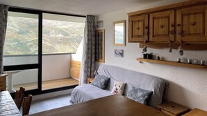 A room with a large window, wooden cabinets, a sofa, and a dining table. - Renovated Studio for 4 People Les Menuires – Ski-in/Ski-out with Direct Access to the Slopes – Brelin (Les Belleville)