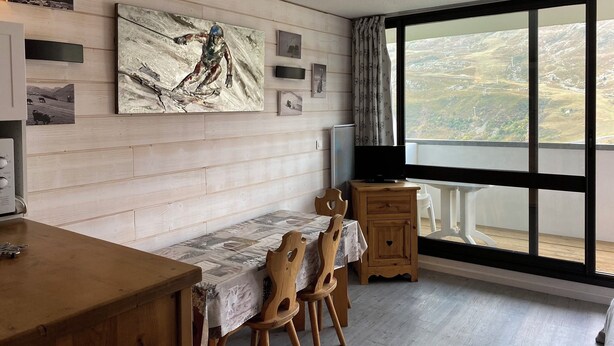 A dining area with a wooden table and chairs, a television, and a large window with a view of a hilly landscape. - Renovated Studio for 4 People Les Menuires – Ski-in/Ski-out with Direct Access to the Slopes – Brelin (Les Belleville)