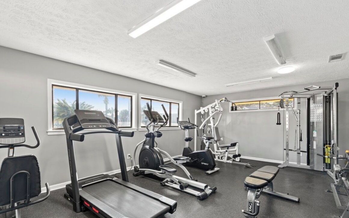 Une salle de sport équipée de tapis de course, de vélos elliptiques, d’un banc et de matériel de musculation.