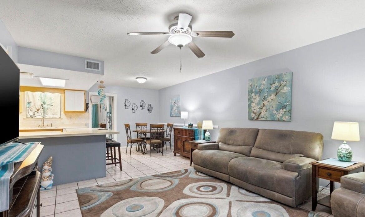 A living room with a sofa, a TV, a ceiling fan, and a dining area with chairs and a table.