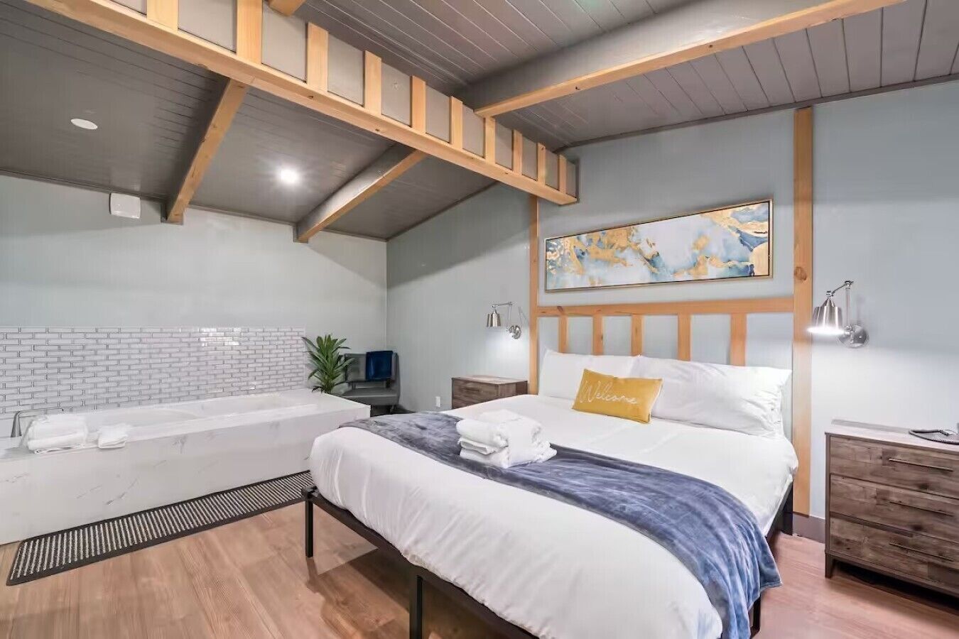 A modern bedroom with a large bed, a built-in bathtub, and a wooden ceiling structure.