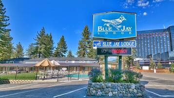 Une enseigne du Blue Jay Lodge indiquant « complet », entourée d’un mur de pierres, d’une piscine et d’une zone délimitée par une clôture, avec un bâtiment visible au fond.