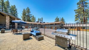 An outdoor patio with seating, a grill, and a stone building in the background.