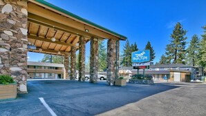 A Blue Jay Lodge with a stone facade, covered parking area, and a clear blue sky.