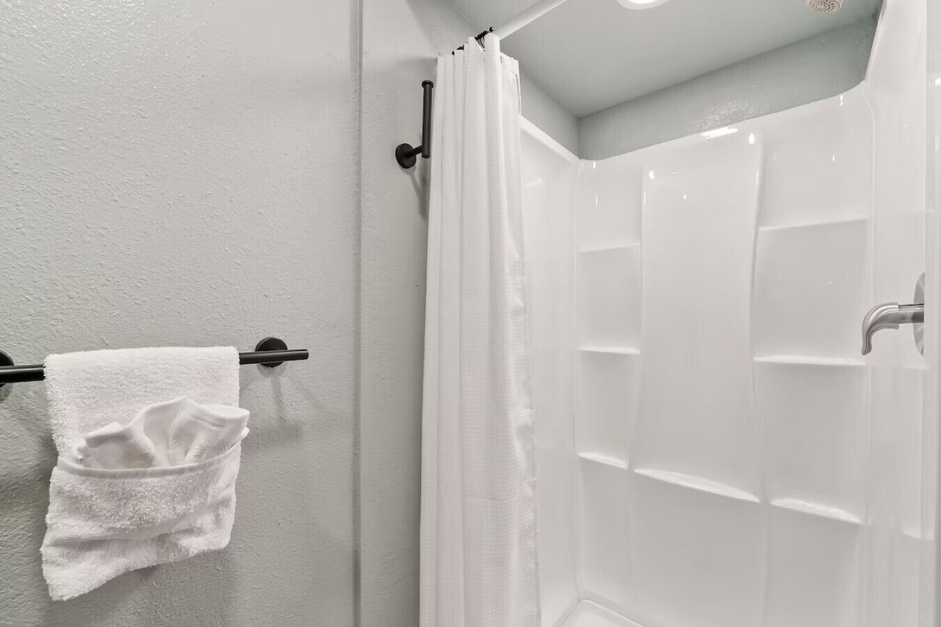 Une salle de bain avec une douche blanche, un porte-serviettes avec une serviette blanche et un mur blanc.