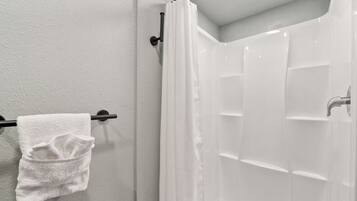 Une salle de bain avec une douche blanche, un porte-serviettes avec une serviette blanche et un mur blanc.