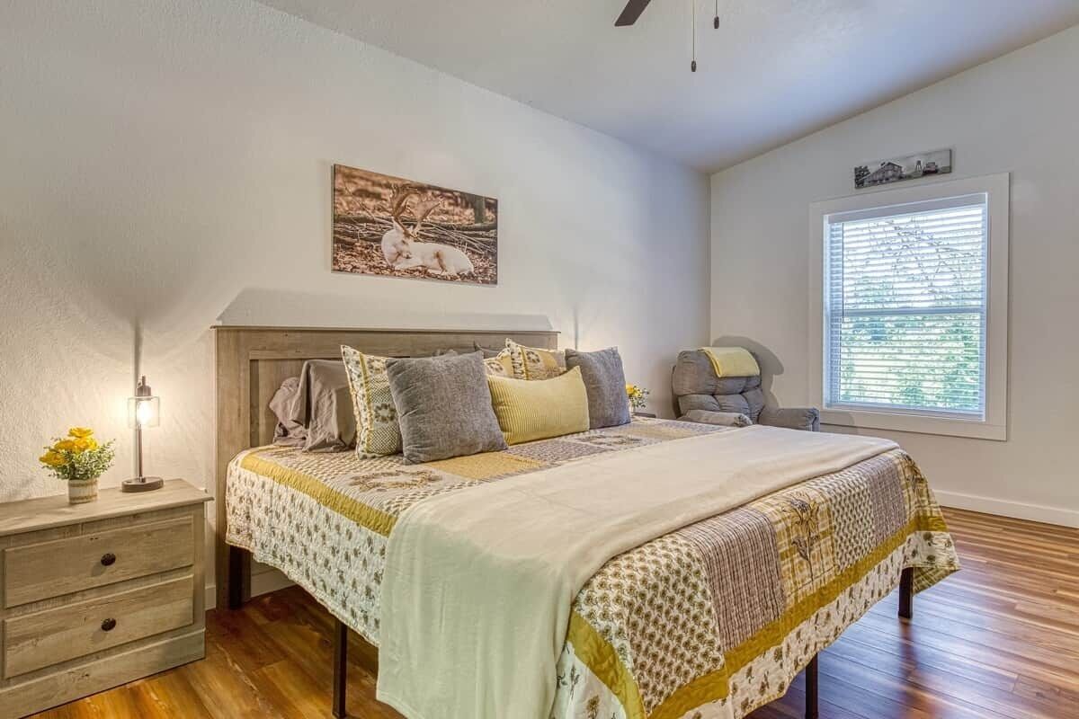 A bedroom with a bed, bedside table, lamp, and a window with blinds.