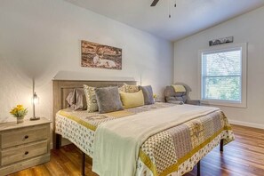 A bedroom with a bed, bedside table, lamp, and a window with blinds.