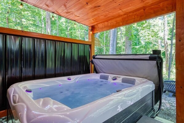 A hot tub with a wooden ceiling and a view of trees outside.