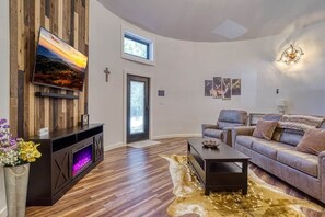 A modern living room with a flat-screen TV mounted on a wooden panel wall, a leather sofa, a coffee table, and a fireplace with a glowing fire.