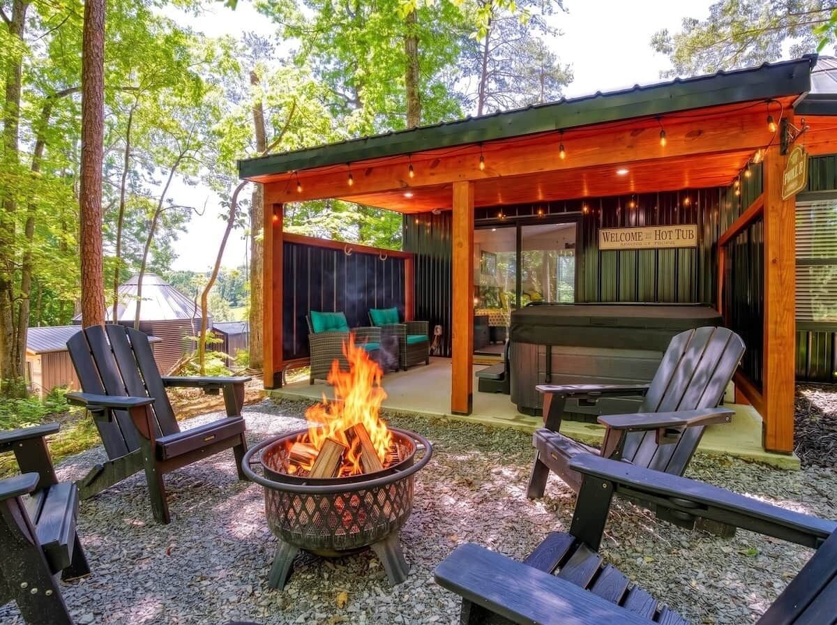 Ein überdachter Außenbereich mit Adirondack-Stühlen, einem Feuerkorb und einem Schild mit der Aufschrift 'Welcome Hot Tub'.