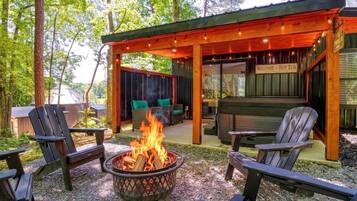 Ein überdachter Außenbereich mit Adirondack-Stühlen, einem Feuerkorb und einem Schild mit der Aufschrift 'Welcome Hot Tub'.