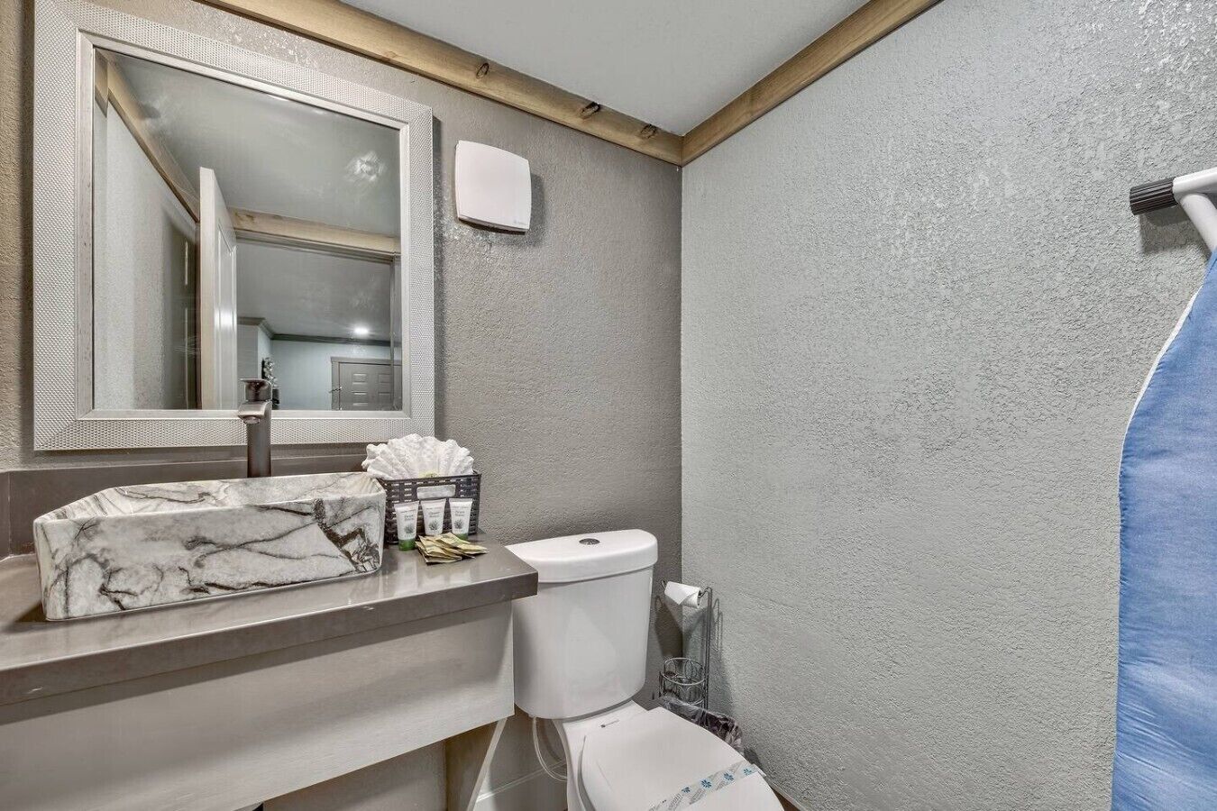 Une salle de bain avec un lavabo en marbre, des toilettes, un rideau de douche et un miroir.