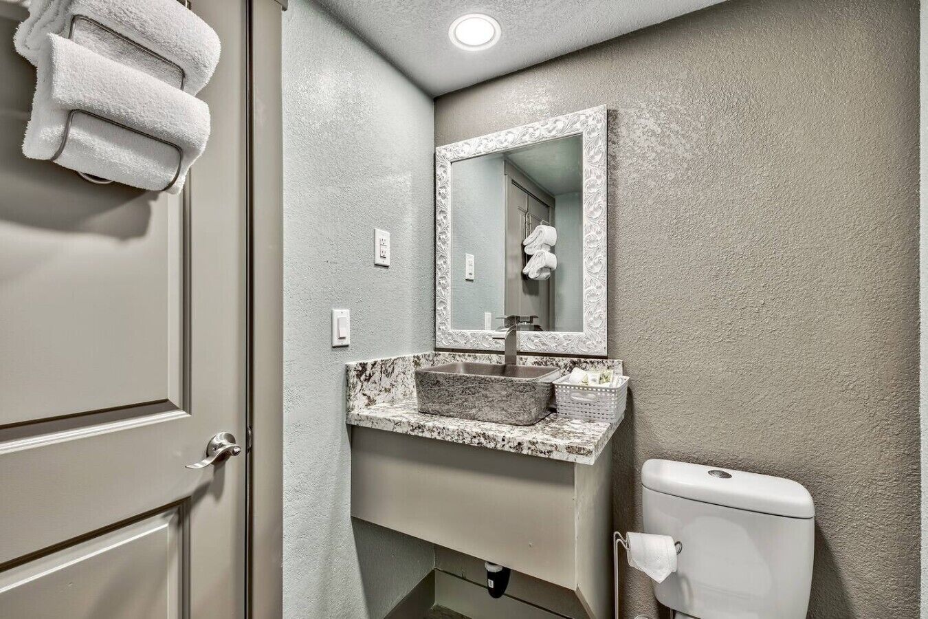 A bathroom with a marble sink, a toilet, and a mirror with an ornate frame.