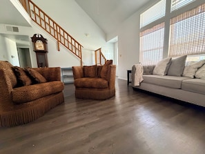 Amplia sala de estar con una escalera de madera, un sofá y un sillón estampado.