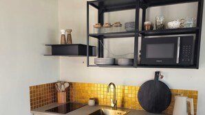 A compact kitchen with a built-in microwave, a sink, and a shelf above the counter. - Syros House - Suite: Slow Living by the Sea, Private Terrace, Ocean Views (Azolimnos)