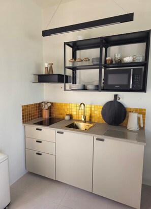 A compact kitchen with a built-in microwave, a sink, and a shelf above the counter. - Syros House - Suite: Slow Living by the Sea, Private Terrace, Ocean Views (Azolimnos)