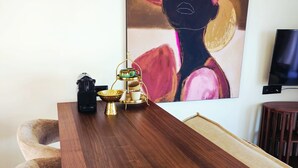 A dining area with a wooden table, chairs, a coffee station, a painting, and a television. - Syros House - Suite: Slow Living by the Sea, Private Terrace, Ocean Views (Azolimnos)