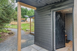 A modern building with a dark exterior, a wooden porch, and a gravel pathway leading to a door.