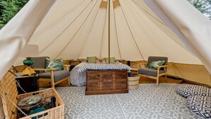 Ein gemütliches Zeltinnere mit einem Bett, zwei Stühlen, einem kleinen Tisch und einer Aufbewahrungsbox.