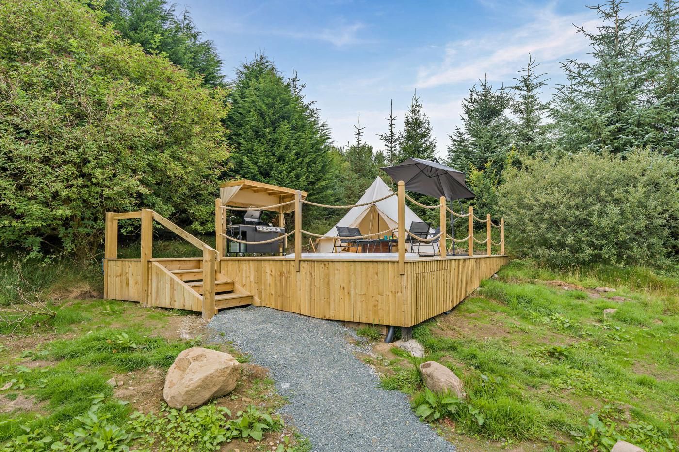 A wooden deck with a grill, seating area, and a tent structure.