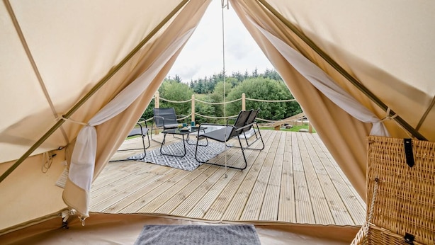 Ein Zelt mit Blick auf eine Terrasse, zwei Stühle und einen Tisch.